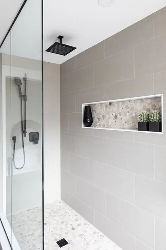 Tiled shower with a recessed shelf and dark showerhead at Caldwell II