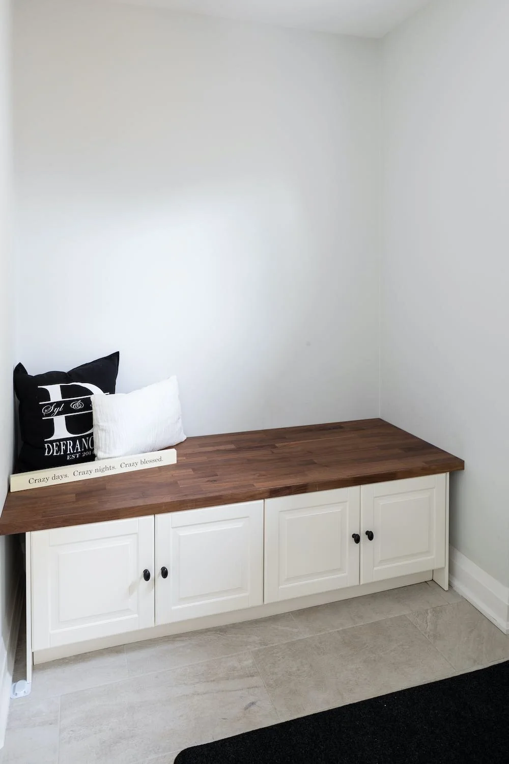 Built-in entry bench with a wood seat and white storage cabinets at Devlin I