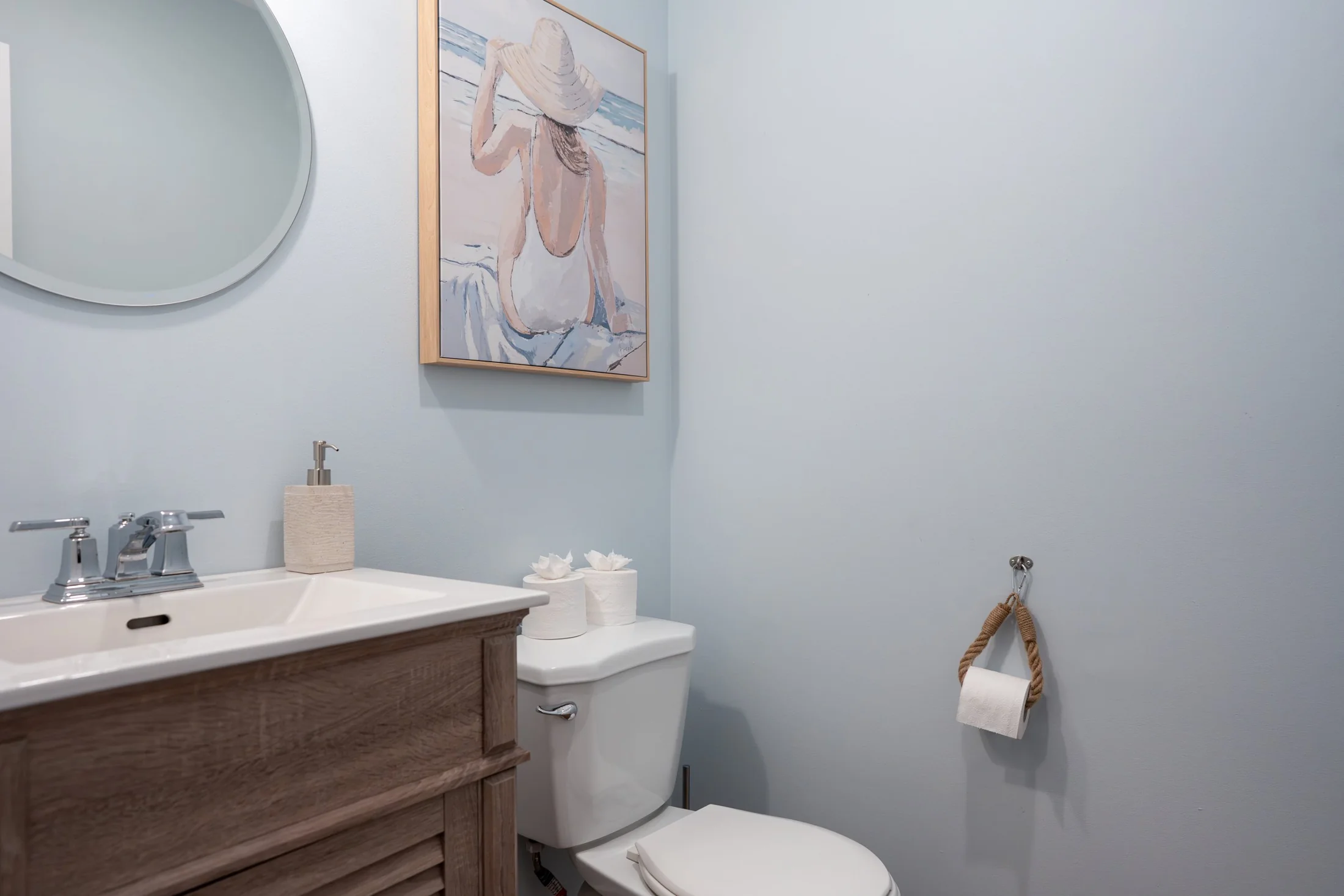 Bathroom with a wood vanity, round mirror and pale blue walls at Joseph I