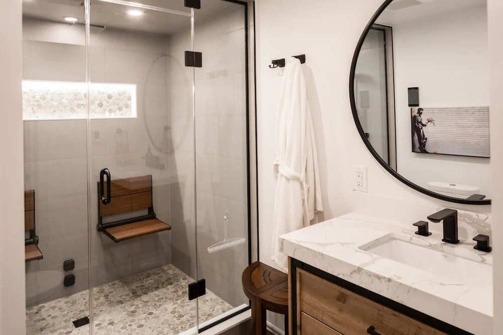 Bathroom with a wood vanity, round mirror and glass shower enclosure at Kingsridge I