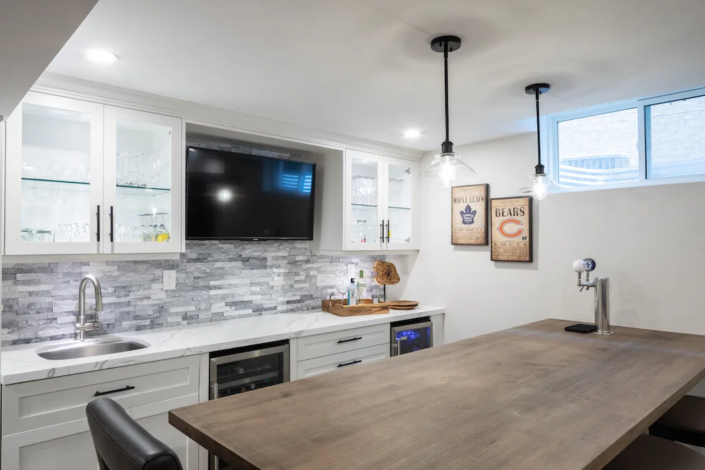 Basement bar with a wood counter, pale cabinets and tile backsplash at Kingsridge I
