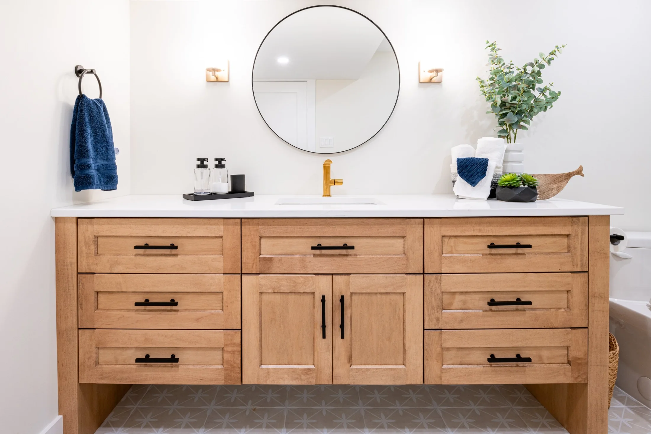 Wood bathroom vanity beneath a round mirror with a brass-coloured faucet at Mill Creek I